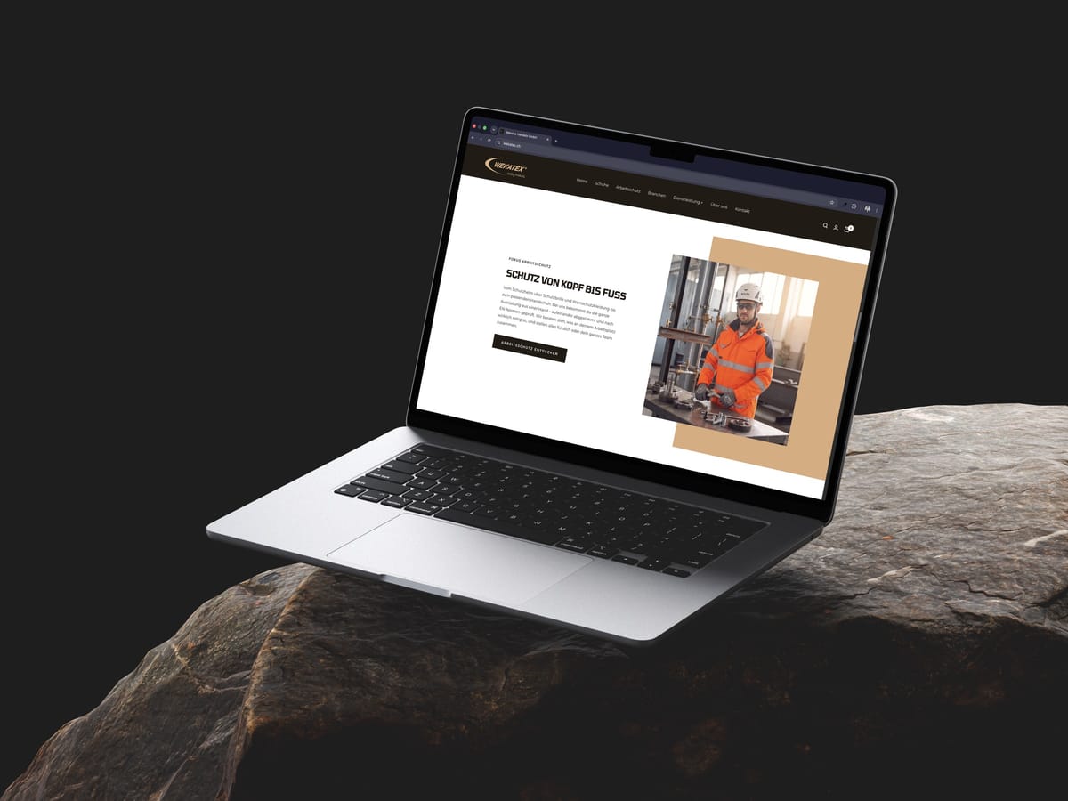 MacBook Air seitlich auf braunem Fels: Bereich «Schutz von Kopf bis Fuss» im Wekatex-Webshop mit Arbeiter in Warnschutzkleidung, im Sand- und Braunton der Marke Wekatex.